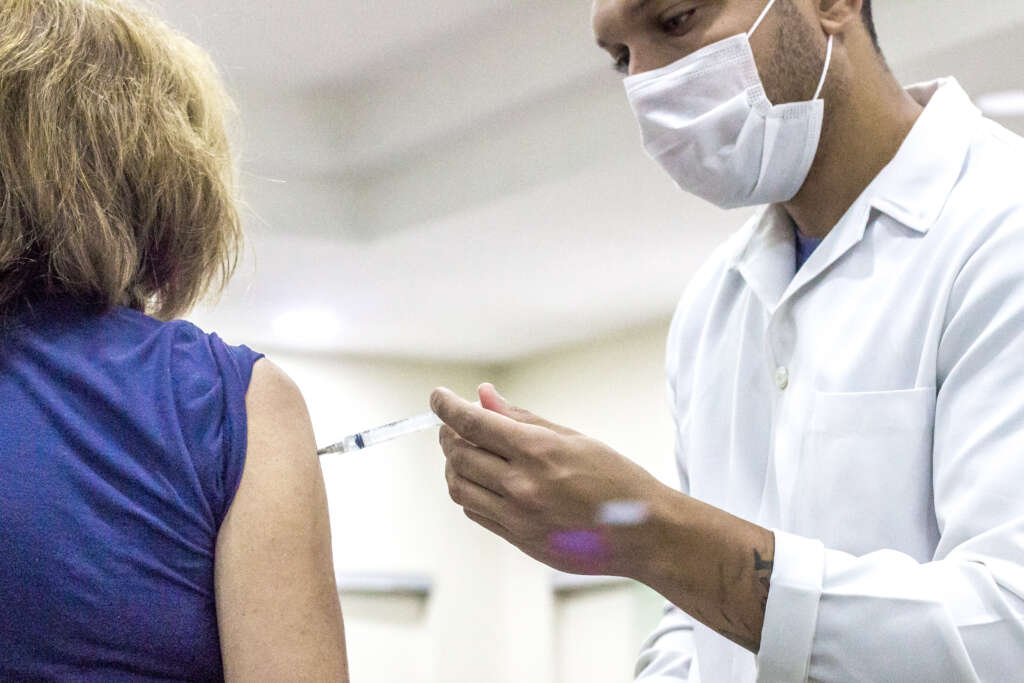 Profissional de saúde aplicando vacina em uma mulher em um CRIE (Centro de Referência de Imunobiológicos Especiais)