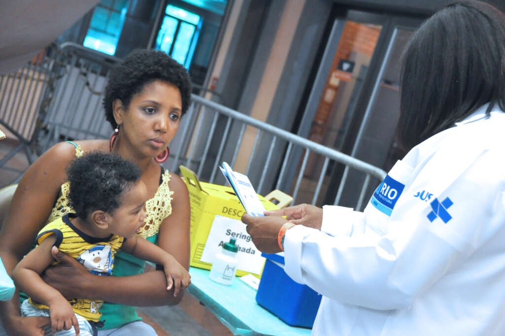 Mãe com seu bebê recebendo orientações de uma profissional de saúde no CRIE (Centro de Referência de Imunobiológicos Especiais)